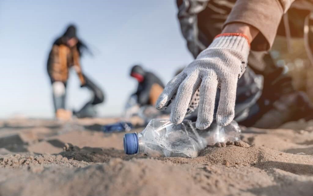 Ein Freiwilliger, der sich für den Umweltschutz einsetzt und eine weggeworfene Plastikflasche am Strand aufhebt, um die Sauberkeit zu fördern und die Verschmutzung zu verringern.