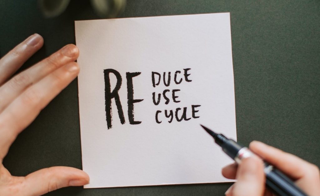 Eine Person hält ein Papier in der Hand und schreibt mit einem Stift die Worte "reduzieren, wiederverwenden, recyceln", um die Bedeutung der ökologischen Nachhaltigkeit zu betonen.